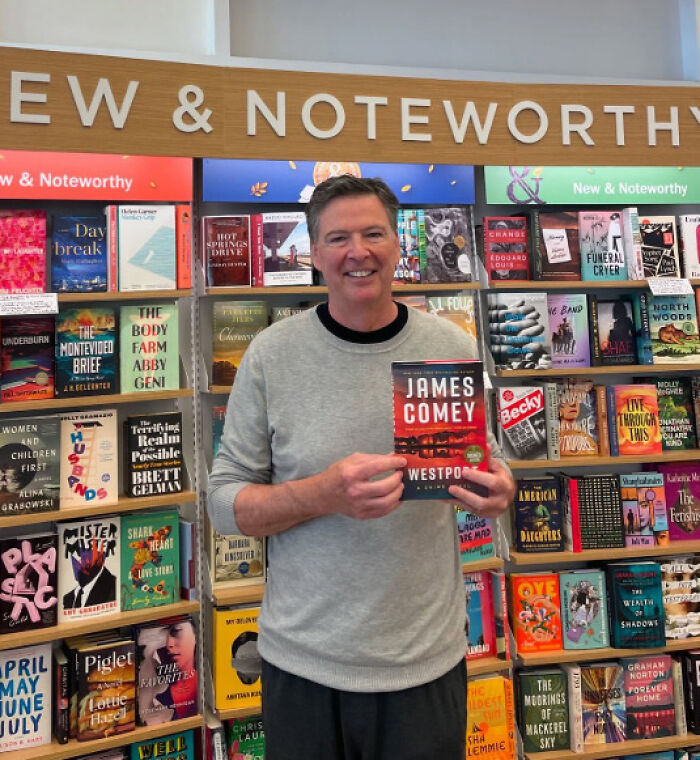 James Comey holding his book in a bookstore section with a new and noteworthy books sign above.