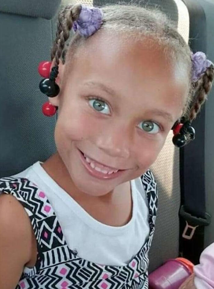 Young girl with bright eyes and braided hair sitting in a car seat, highlighting child trafficking and exploitation concerns.