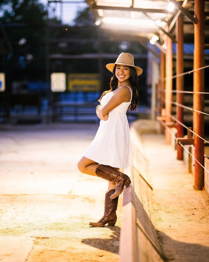 College student posing outdoors in a white dress and cowboy boots, facing potential deportation after illegal turn at red light.