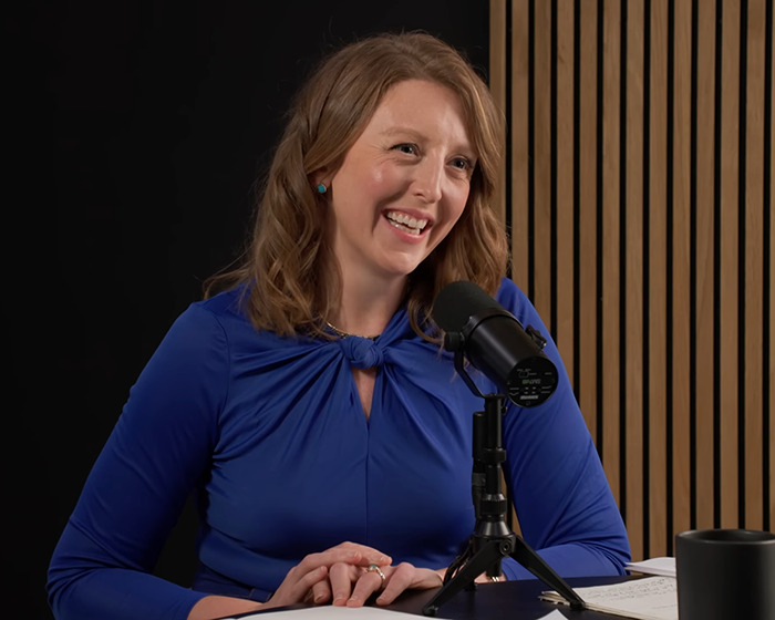 Wellness influencer in blue blouse speaking into microphone during a podcast, linked to new surgeon general nomination news.