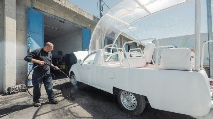 Man cleaning Pope Francis&rsquo; Popemobile being converted into a mobile health unit for Gaza children in an outdoor garage.