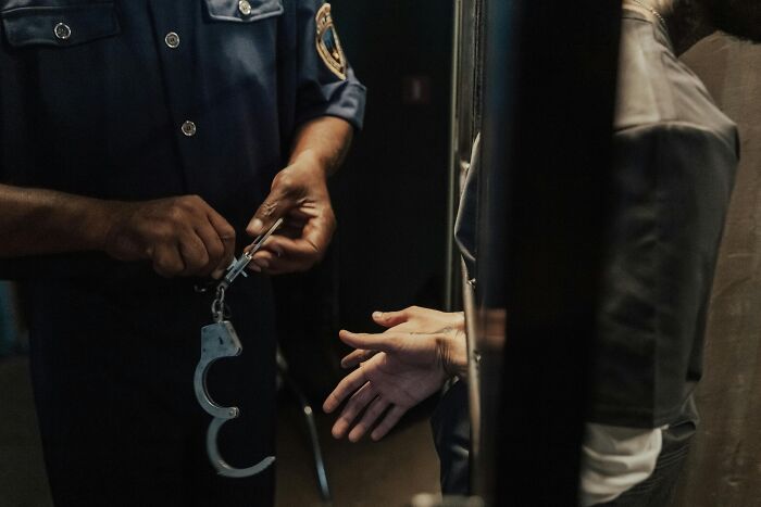 Police officer holding handcuffs near a suspect's outstretched hands in a dimly lit cell, related to hostage situation.