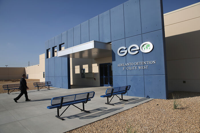 Exterior of a GEO private prison facility with benches outside under clear sky linked to Trump&rsquo;s private prison pals and migrant crackdowns.