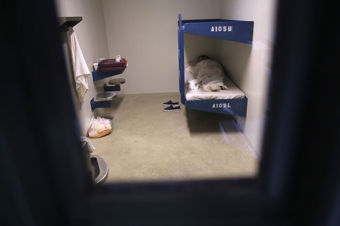 Prison cell interior with bunk beds and personal items, highlighting private prison and migrant crackdown concerns.