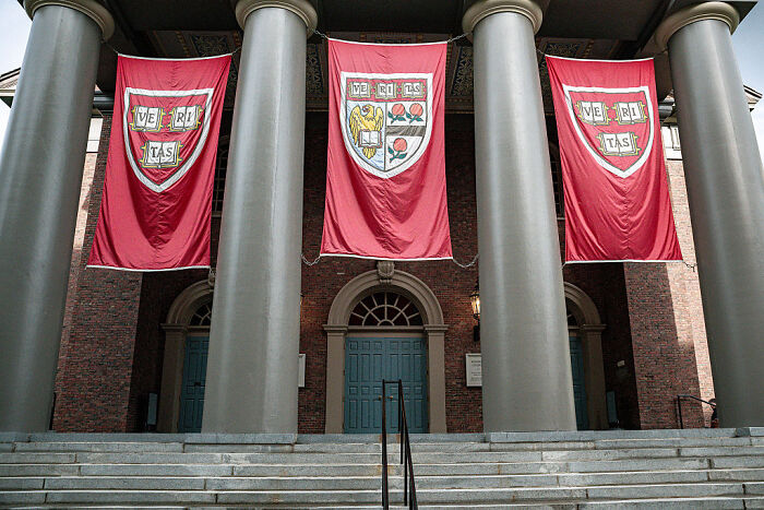 Harvard University building entrance with pillars and red banners, symbolizing student visa freeze and social media scrutiny.