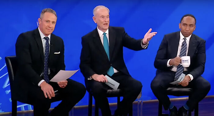 Three male news anchors in suits seated on stage during a town hall reacting to Trump&rsquo;s first 100 days claims.