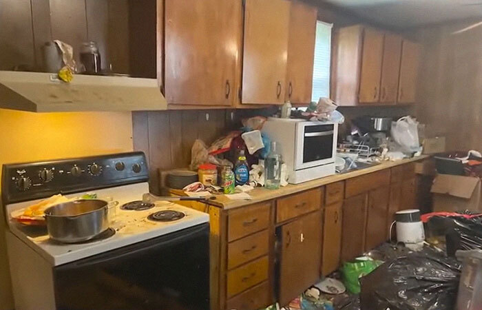 Cluttered and filthy kitchen in a home with over 40 animals and a rotting goat carcass visible among the mess.