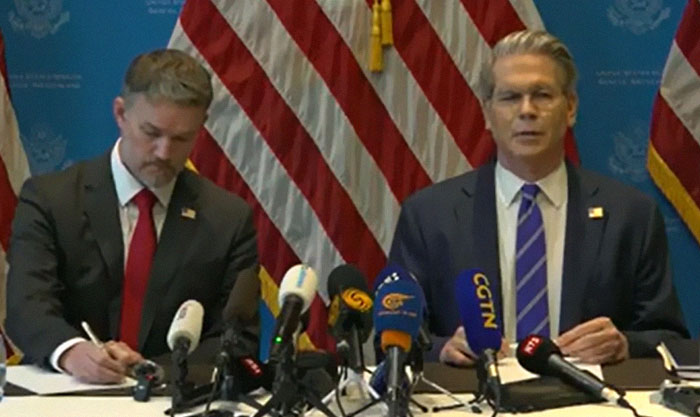Two officials at a press conference discussing the U.S. and China deal to cut tariffs, with multiple microphones in front.