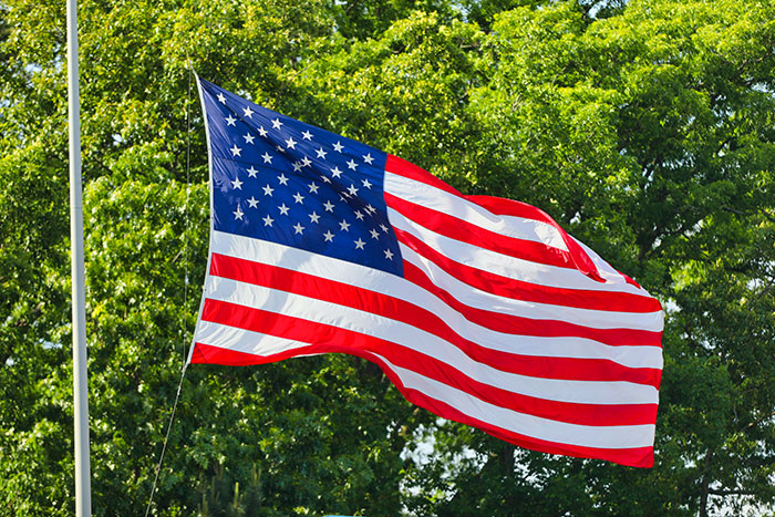 American flag waving outdoors amid green trees representing U.S. and China tariff cut deal announcement
