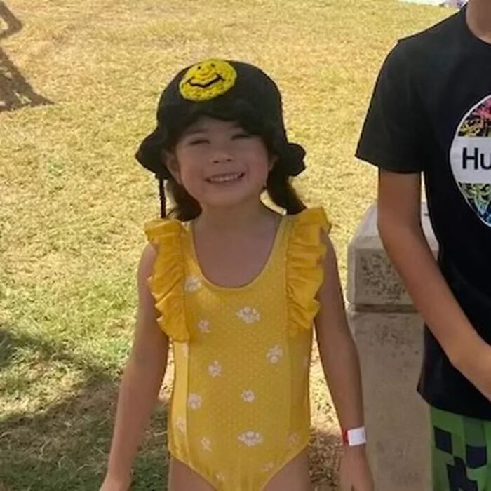Young girl smiling outdoors wearing yellow swimsuit and black hat, related to fatal shooting involving brother and dad&rsquo;s rifle at home.