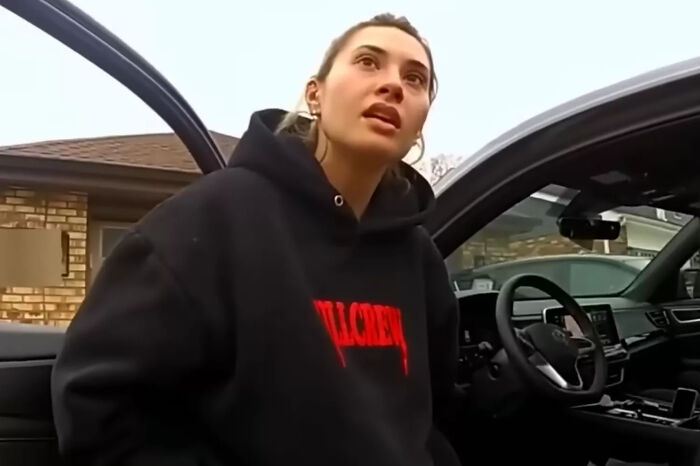 Woman in black hoodie standing by car door, related to teacher accused of multiple sexual acts with pupil at school case.