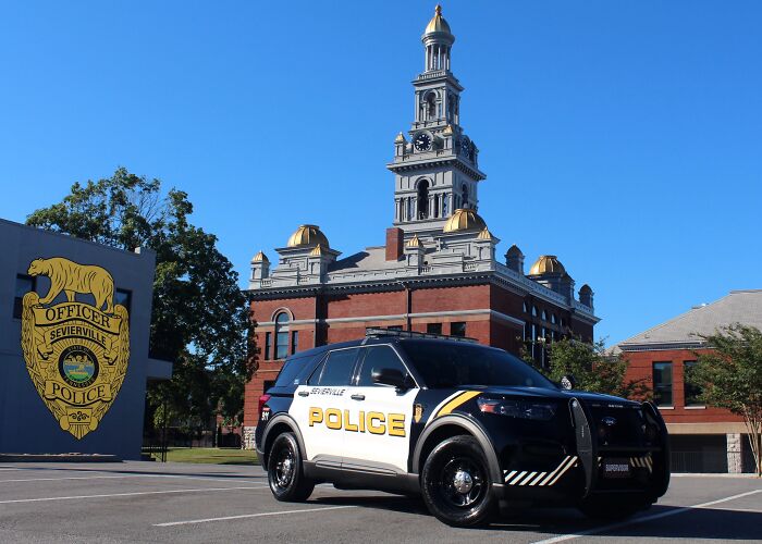 Sevierville police vehicle parked near courthouse with police badge mural in the background under clear blue sky.