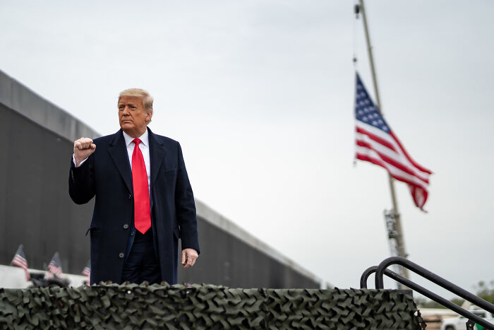 Former President Trump standing near military vehicle with American flag, symbolizing control of National Guard forces.
