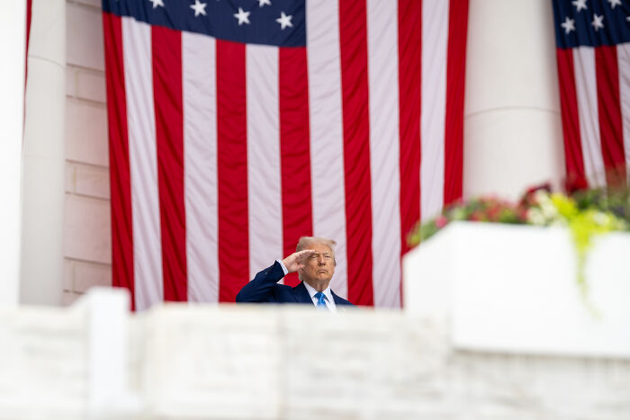 Former President Trump saluting in front of large American flags during announcement of travel ban.
