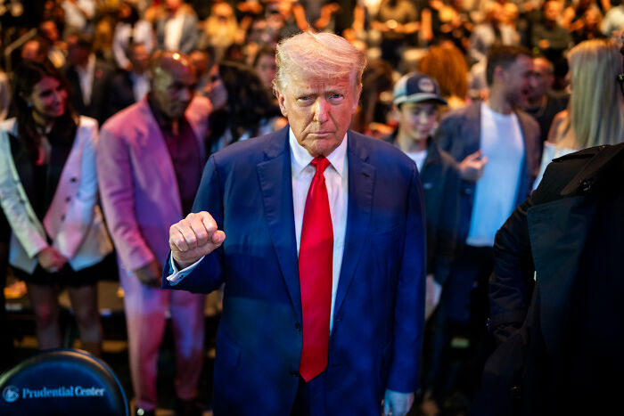 Donald Trump in a suit and red tie raising fist amid crowd during event related to California Governor Gavin Newsom arrest discussion