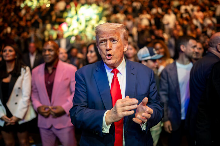 Man in a blue suit and red tie clapping at a crowded event, highlighting MAGA&rsquo;s hypocrisy in viral Obama video.