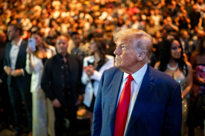 A man in a blue suit and red tie at a crowded event, related to Elon Musk walking back Trump criticism.