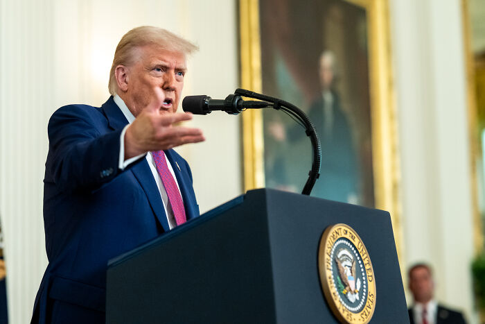Former U.S. president speaking at a podium with presidential seal about foreign student visas and social media access.
