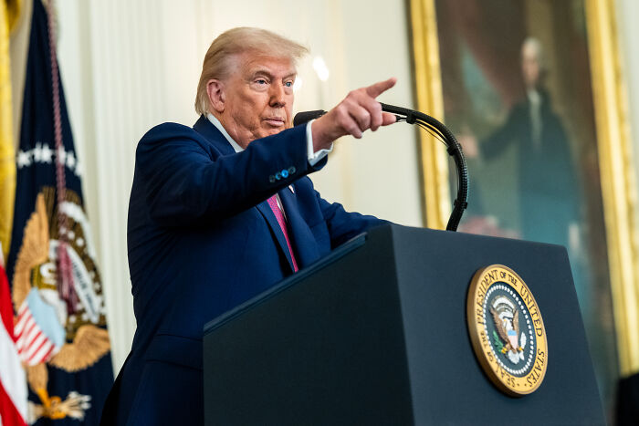 Former President Trump speaking at a podium with presidential seal, related to NIH grants reinstatement and legal ruling.