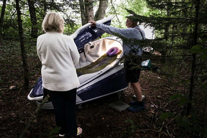 Two people examining a Sarco pod euthanasia capsule in a wooded outdoor setting, highlighting the Sarco pod advocate topic.