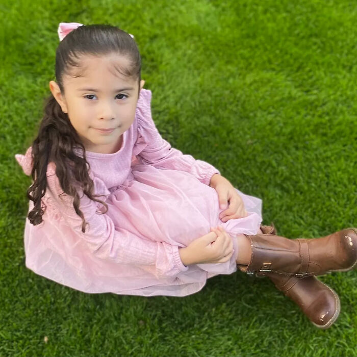 Young girl in a pink dress and brown boots sitting on grass, related to tragic story of fatally shot girl by brother.