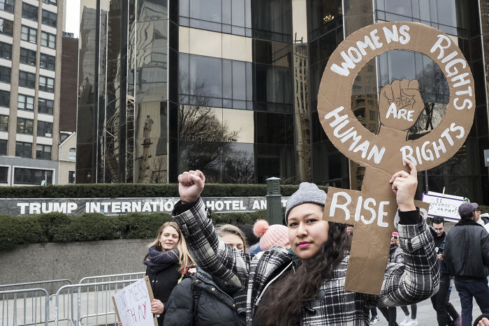 Protesters outside Trump International Hotel with a sign advocating women's rights amid Medicaid Planned Parenthood funding debate.