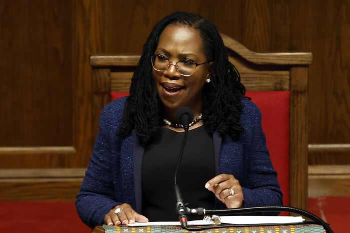 Woman speaking at a wooden podium with microphone, discussing Supreme Court and reverse discrimination in civil rights protections.