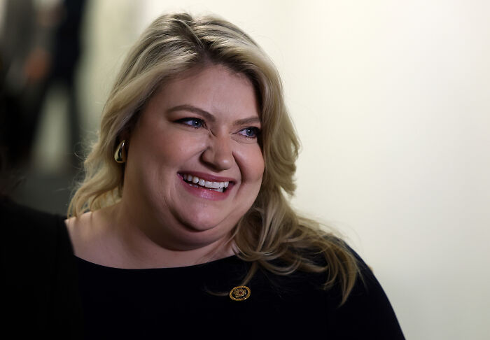 Smiling Florida GOP representative with blonde hair, wearing black, discussing emergency care delay linked to abortion law impact.