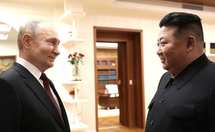 Two men in formal attire smiling and talking indoors, related to North Korea beach resort tourism development plans.