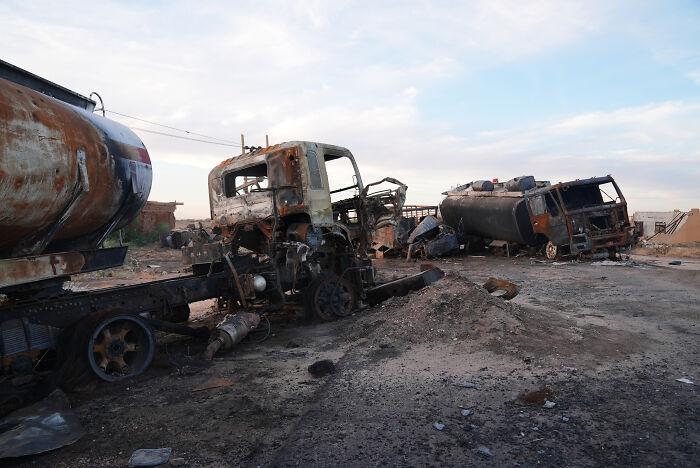 Burned-out trucks and destroyed vehicles in a war-torn area, highlighting deadly wars and humanitarian crises in conflict hotspots.