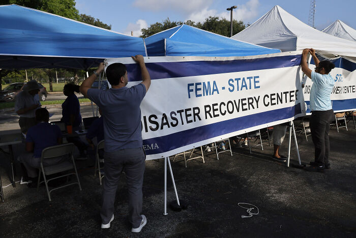 People setting up a FEMA disaster recovery center tent amid hurricane season preparation and staff urgency.