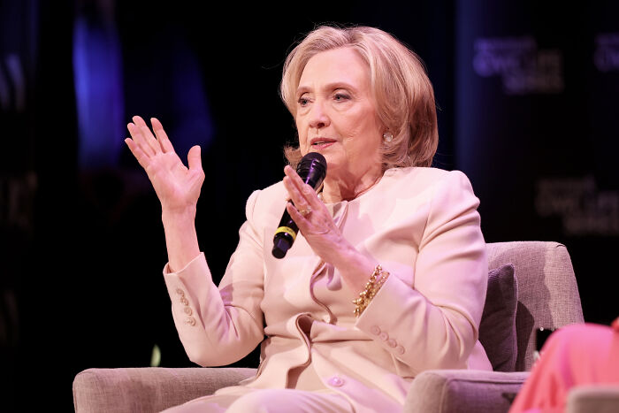 Hillary Clinton speaking into a microphone, discussing politics and criticizing Trump&rsquo;s low-energy birthday parade.