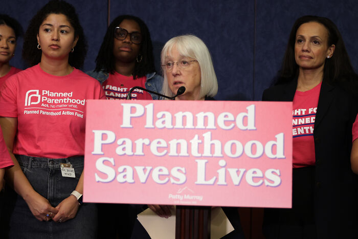 Woman speaking at a Planned Parenthood rally, with supporters wearing pink shirts about Medicaid funding and South Carolina.