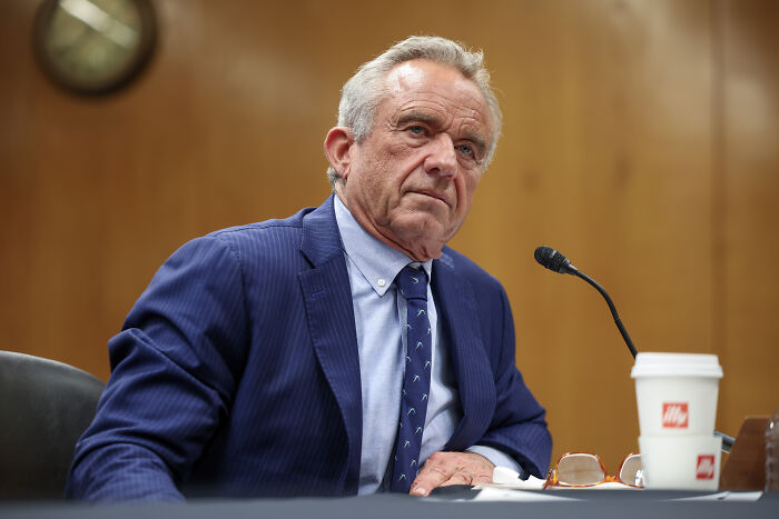 Robert F Kennedy Jr. seated at a microphone in a formal setting, related to CDC vaccine advisory committee news.