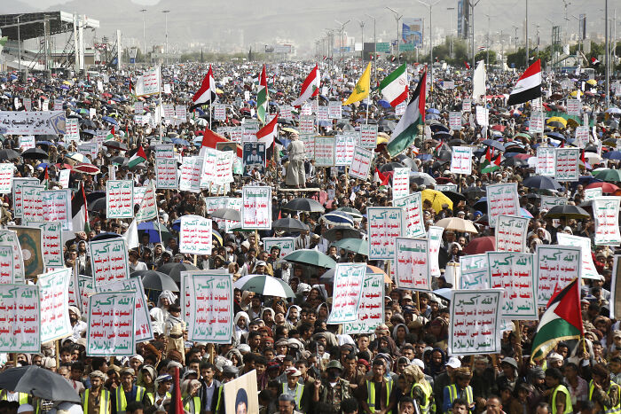 Large crowd of protesters holding flags and signs in a conflict hotspot, highlighting deadly wars and humanitarian crises.