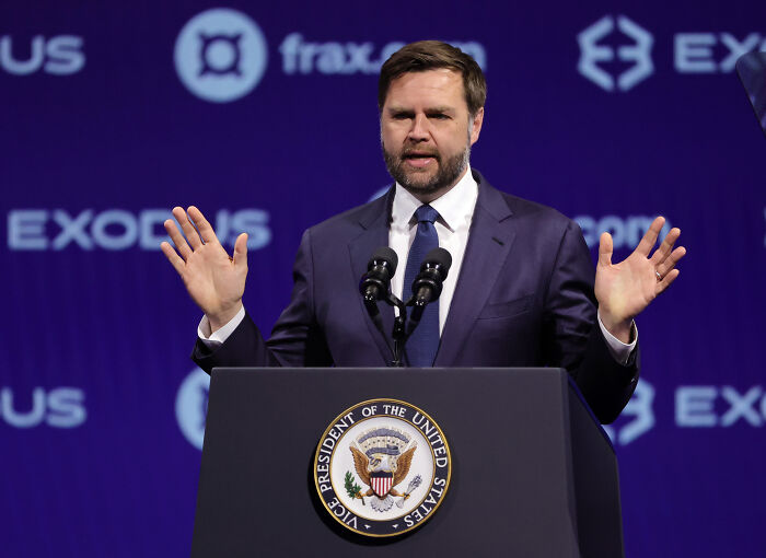 Vice President JD Vance speaking at a podium with Vice President seal, discussing Bluesky platform suspension issue.