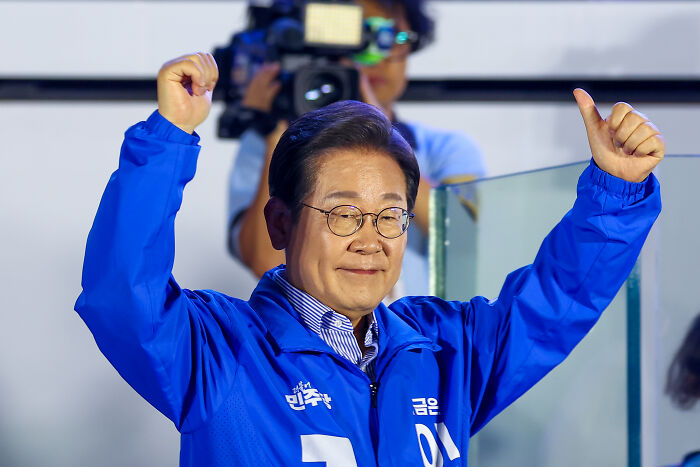 Man in blue jacket raising both fists, representing South Korea, in a moment related to Karoline Leavitt&rsquo;s viral South Korea question.