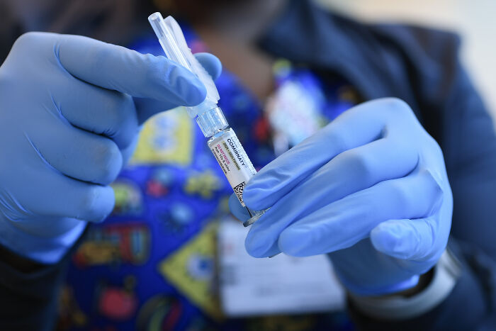 Gloved hands holding a COVID-19 vaccine vial and syringe, related to Robert F. Kennedy Jr. CDC vaccine advisory committee news.