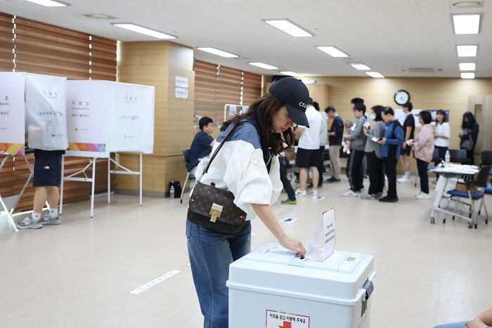 Woman casting vote in a busy polling station, highlighting Karoline Leavitt&rsquo;s cringe binder shuffle over South Korea question.