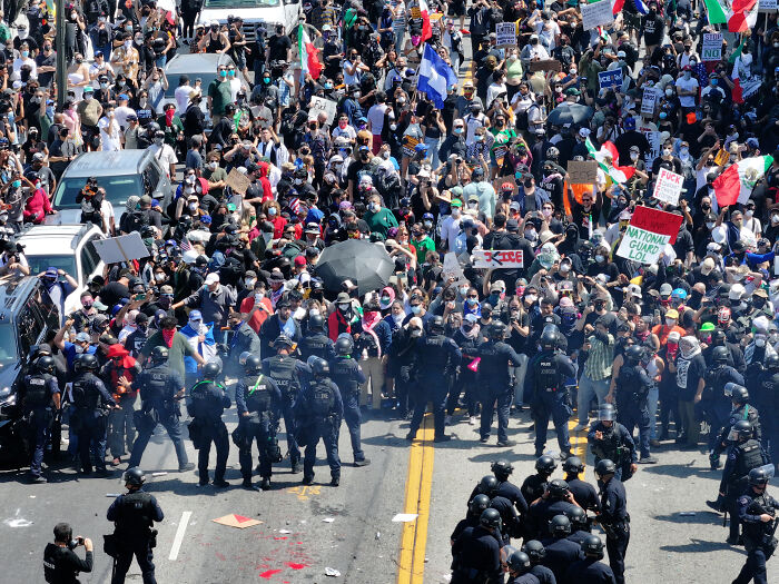 Large crowd and police in riot gear during protest related to National Guard control dispute in California.