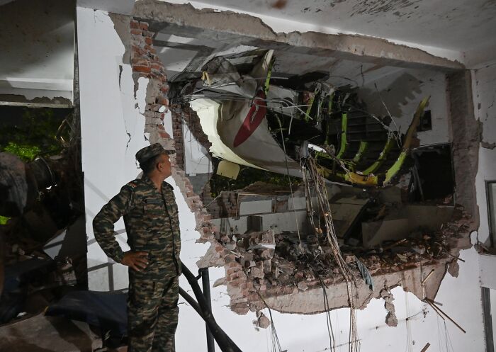 Air India crash wreckage embedded in a building with a soldier inspecting the site, highlighting the miracle lone survivor story.
