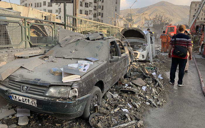 Damaged cars amid rubble in a street after Iran fires 100 drones at Israel causing destruction and emergency response.