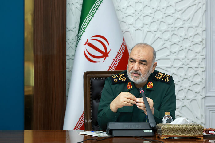 Senior Iranian Revolutionary Guard Corps leader speaking at a conference with Iranian flag visible behind him.
