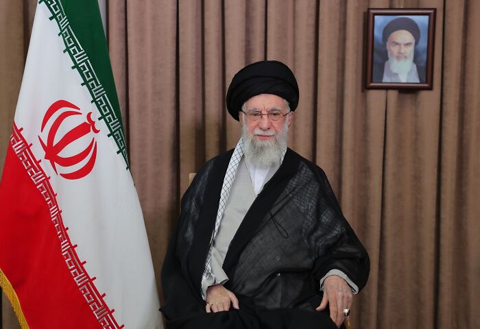 Iran&rsquo;s Supreme Leader seated near the national flag, delivering a serious address amid rising tensions with the U.S. and Israel.