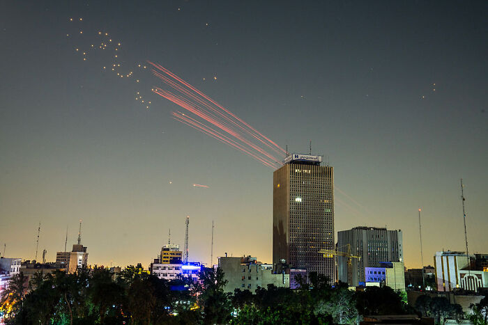 Missile streaks over city skyline at dusk after Israeli strike near Iran State TV building.