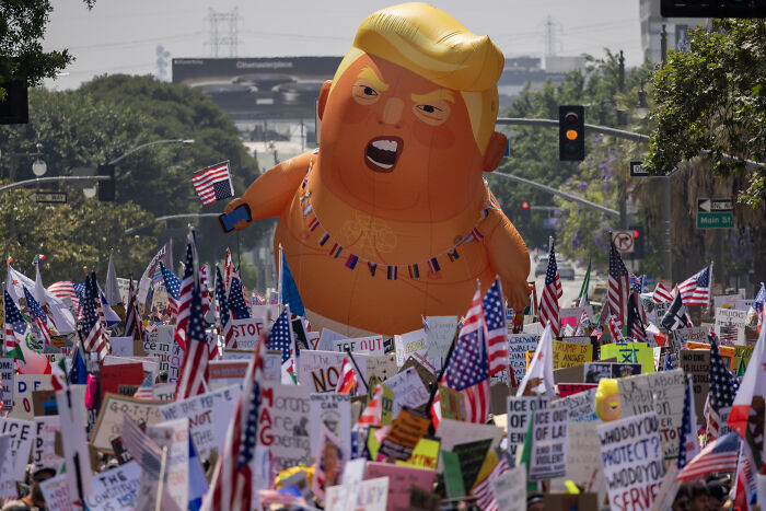 Protest with numerous signs and an inflatable Trump balloon amid discussions on ICE immigration raids in blue cities.