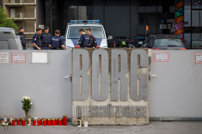 Police officers stand near a van outside BORG school with candles placed in memorial for Austrian shooter incident.
