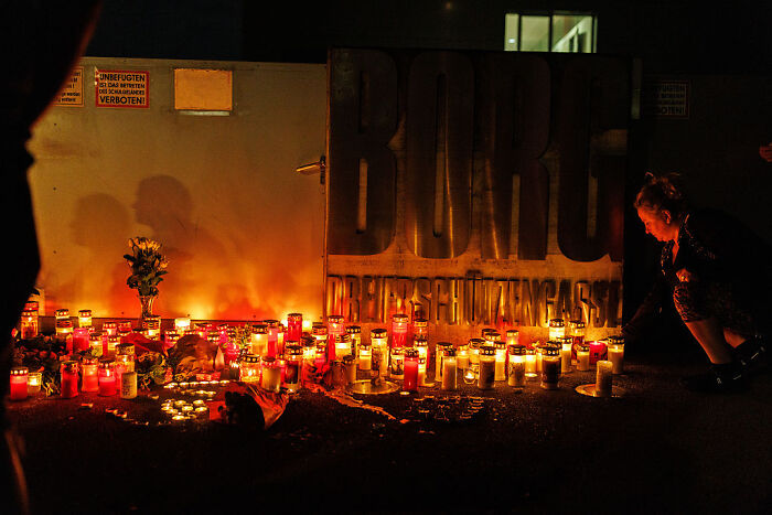 Memorial candles lit at night honoring victims of Austrian shooter incident at a public location with people paying respects.