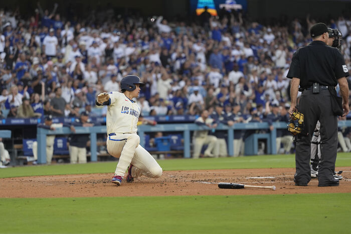 Baseball player in Los Angeles jersey sliding into home plate during a crowded game with a singer wearing Dominican jersey present.