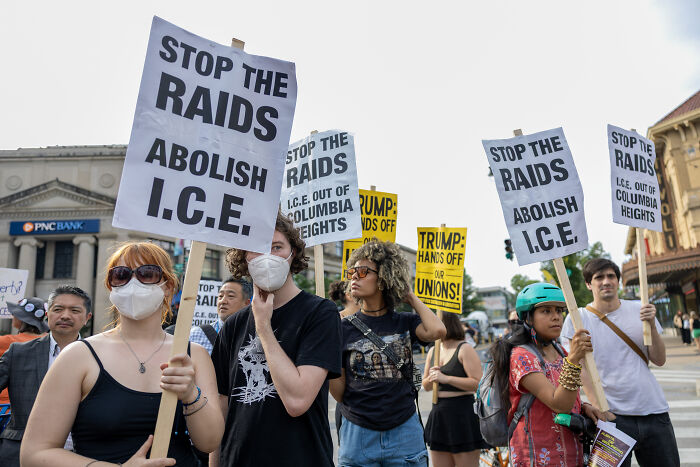 Protesters holding signs against ICE immigration raids in blue cities amid new Trump directive.